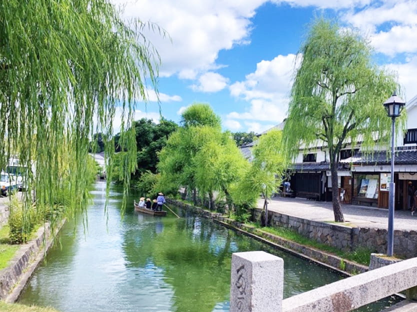 青い空と緑の木々が生い茂る倉敷美観地区内の川を下る船